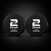 Two closed 2Fresh Hair Clay tins in Tuscan Leather on a dark studio background