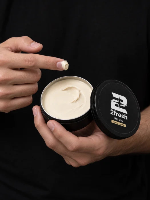 A small amount of ivory 2Fresh Hair Clay on a fingertip above the open tin
